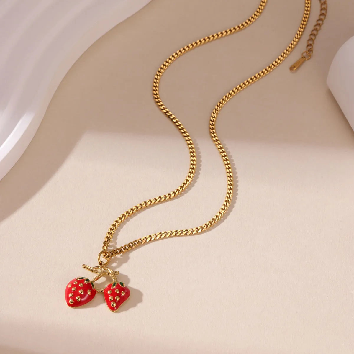 Alloy strawberry fruit pendant necklace on stainless steel chain with red charm and white gradient background.
