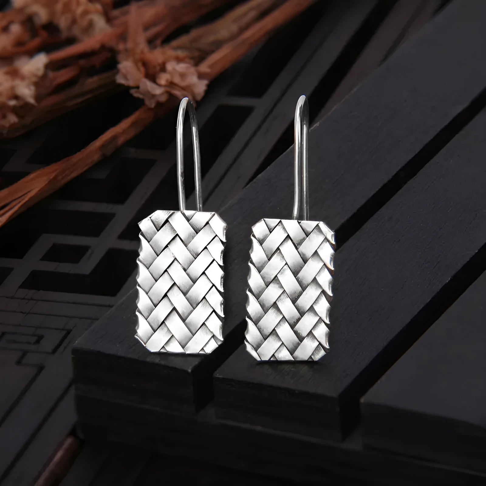 Silver geometric earrings with a woven diamond plaid pattern on a white background.
