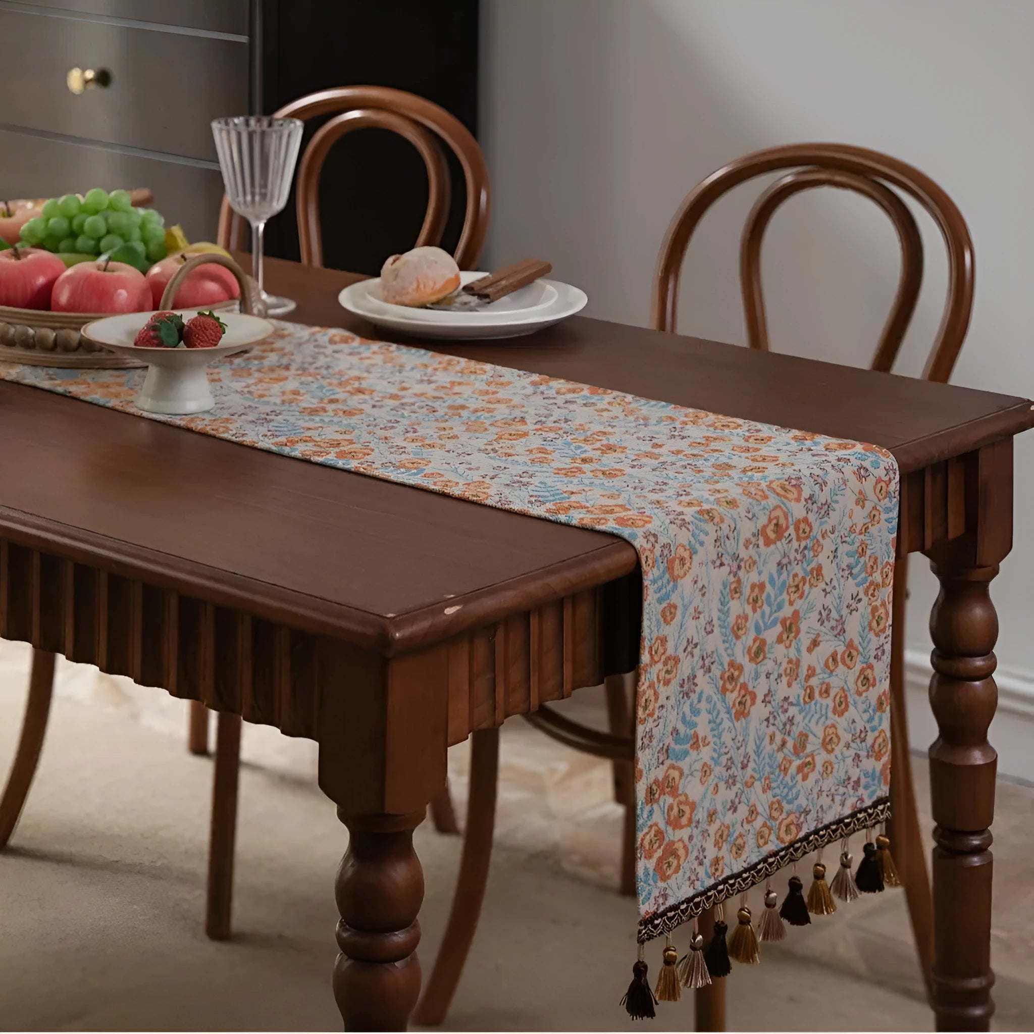 Beige polyester jacquard table runner with long tassels and a floral leaf pattern laid on a table.
