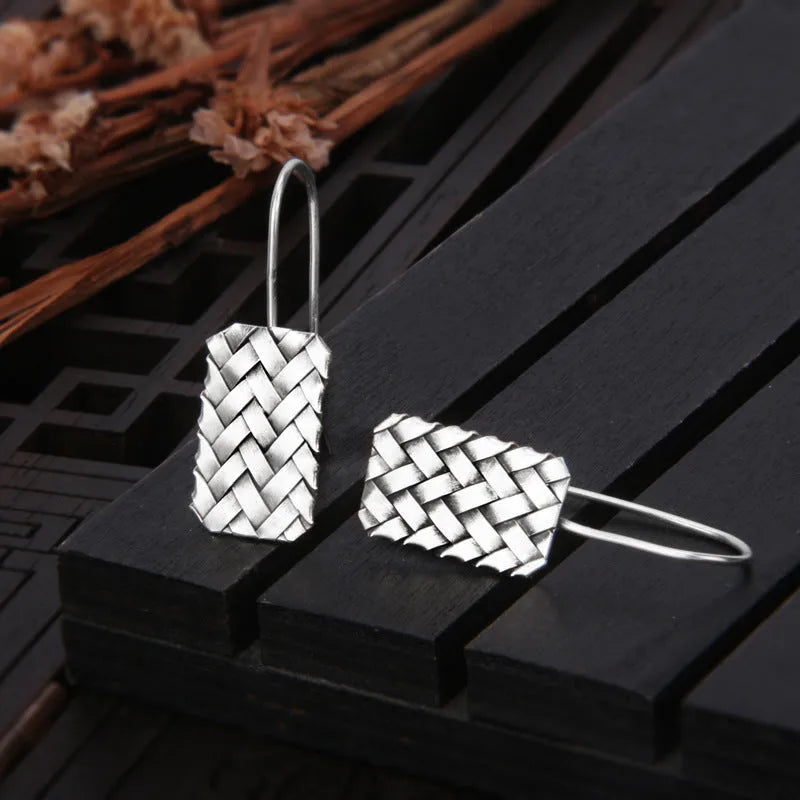 Silver geometric earrings with a woven diamond plaid pattern on a white background.