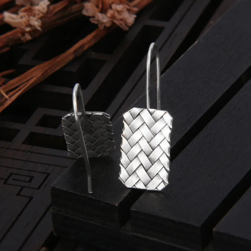 Silver geometric earrings with a woven diamond plaid pattern on a white background.