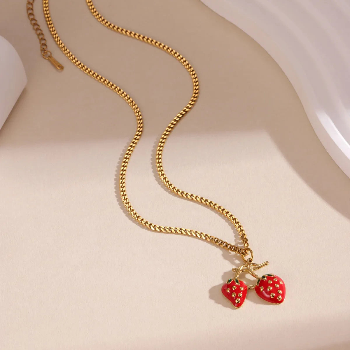 Alloy strawberry fruit pendant necklace on stainless steel chain with red charm and white gradient background.