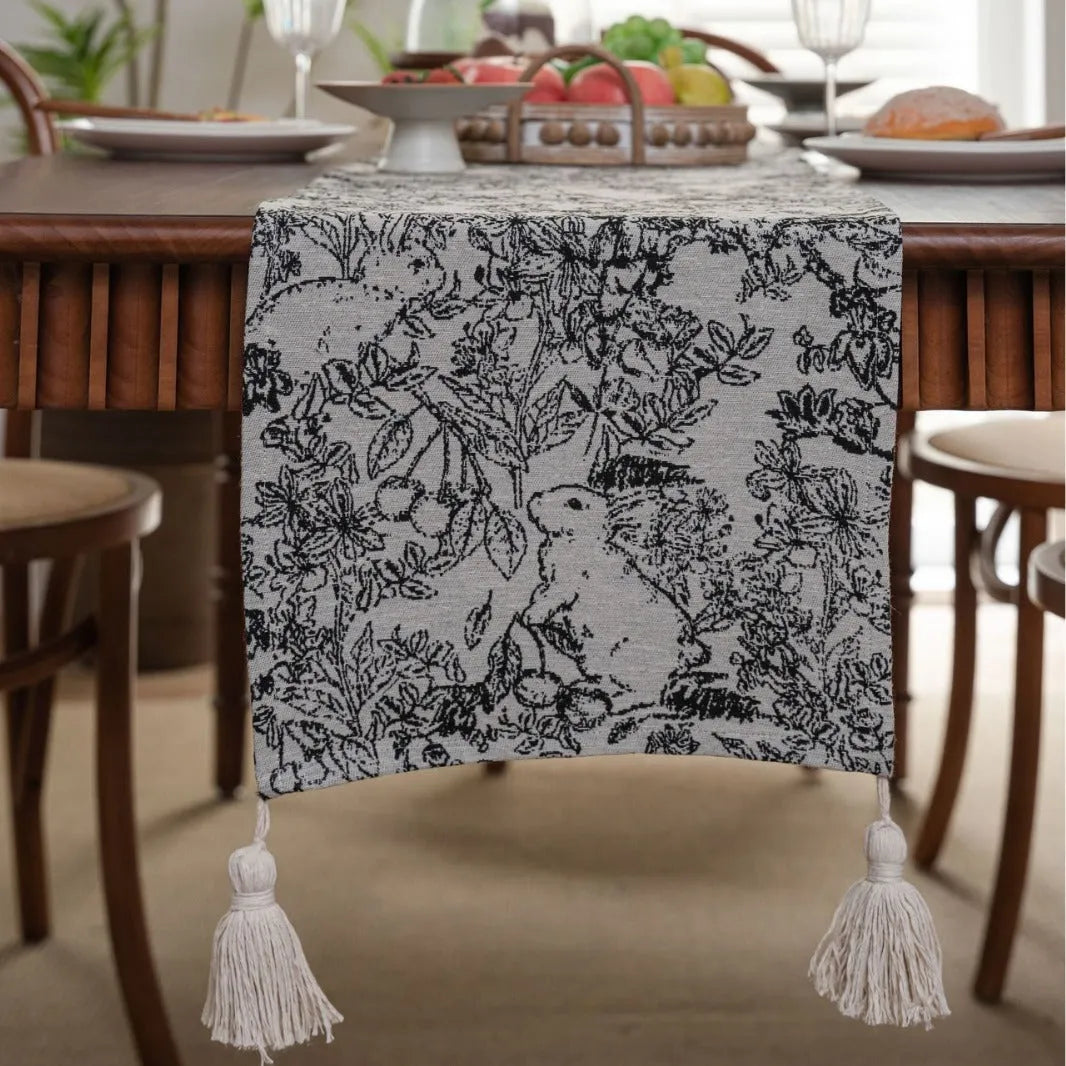 Beige polyester jacquard table runner with long tassels and a floral leaf pattern laid on a table.