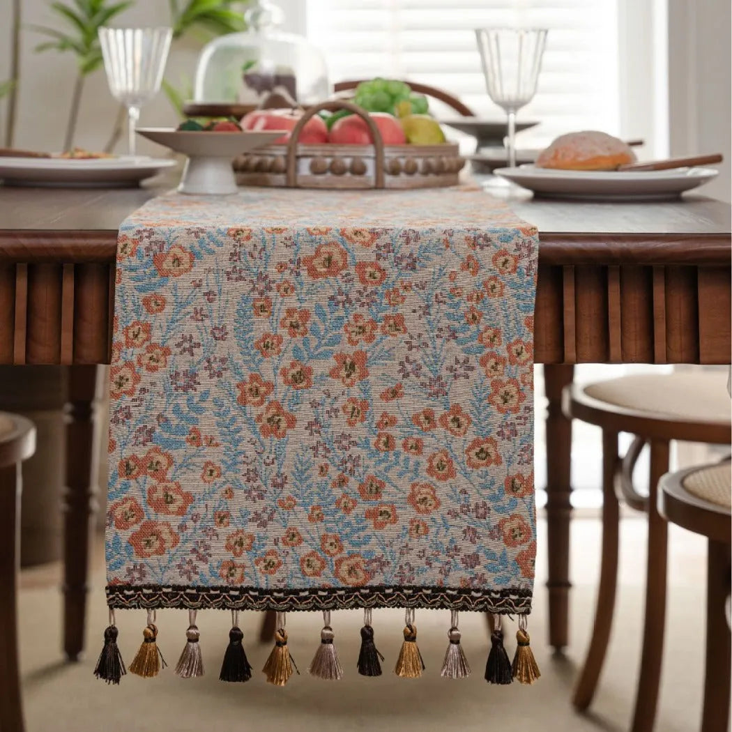 Beige polyester jacquard table runner with long tassels and a floral leaf pattern laid on a table.