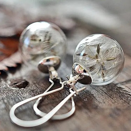 Close-up of transparent glass ball earring with dandelion seed design on a silver French hook.