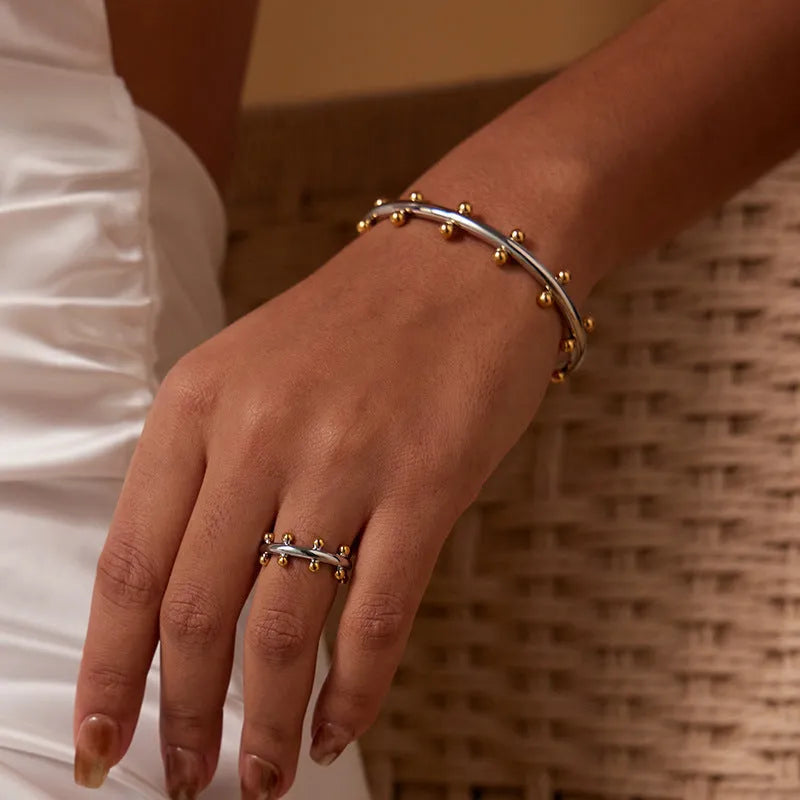 Stainless steel C-shaped bracelet with textured rivet and bean bead design in gold colour.