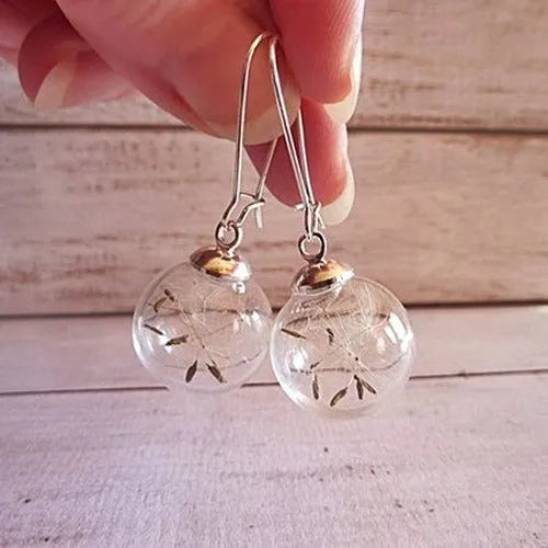 Close-up of transparent glass ball earring with dandelion seed design on a silver French hook.