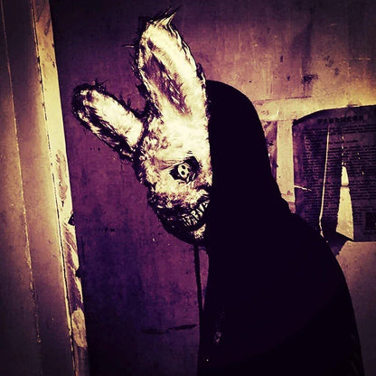 A creepy and realistic plush bunny mask with long pink ears, a bloody mouth, and glowing green eyes - perfect for Halloween and costume parties.