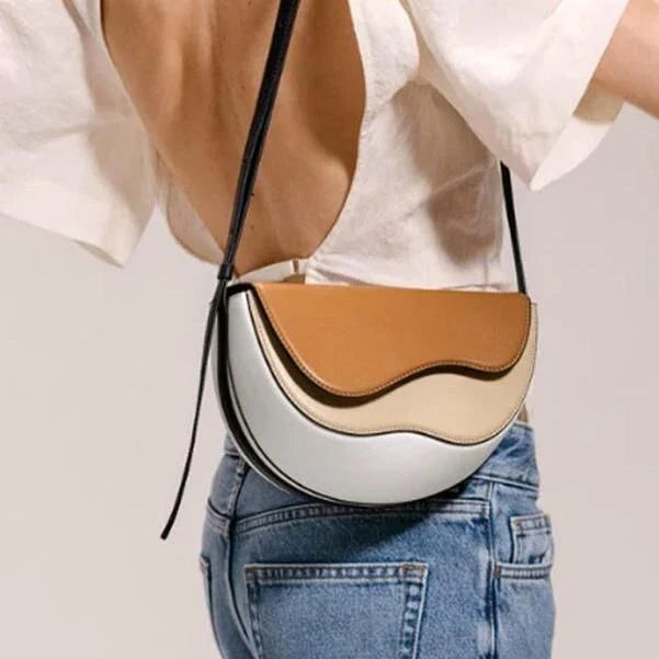 Stylish contrast color crossbody saddle bag with patchwork design, flap closure, and adjustable strap