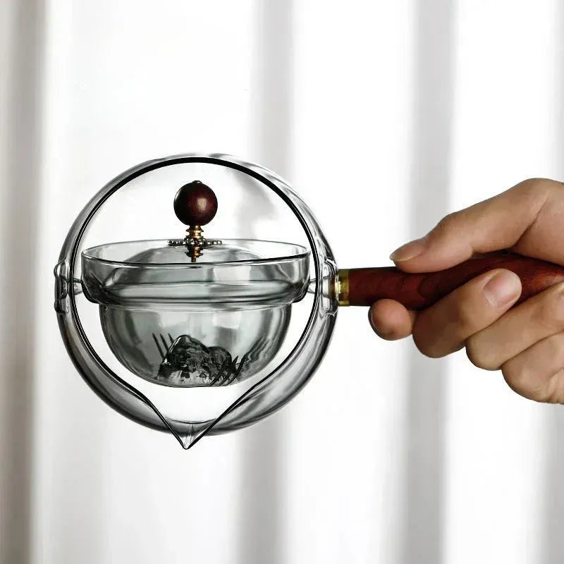 Transparent rotary glass teapot with wooden handle and built-in infuser on countertop