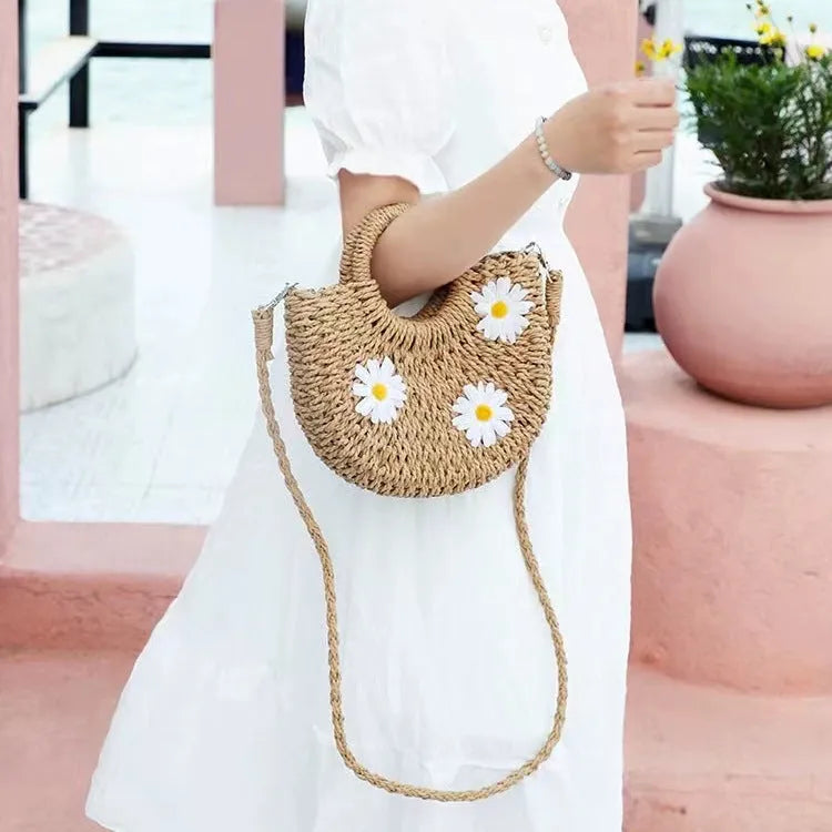 Light brown woven straw crossbody bag with daisy decoration showing shoulder strap