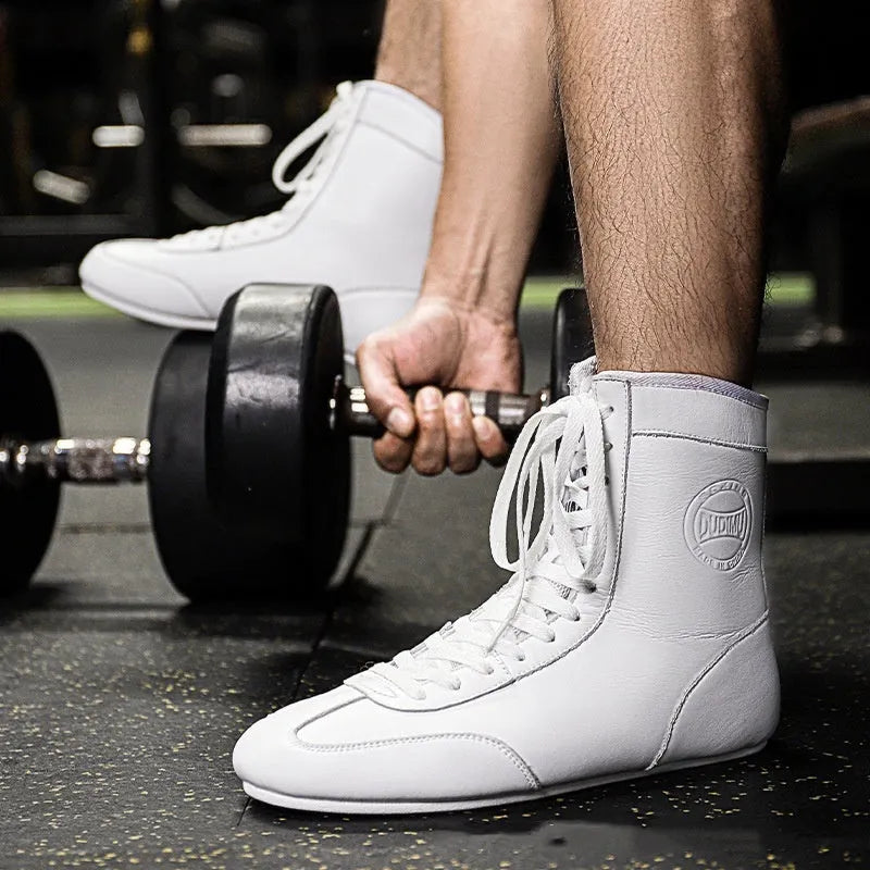 Pair of black and gold professional boxing shoes with mesh panels on a gym floor.