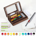 Mini walnut-finish wooden watercolour paint box open to show internal compartments with pigment pans.