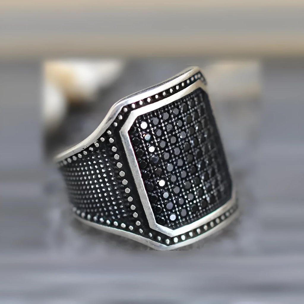 Black alloy ring with copper inlay detail and a central zircon stone on a finger.