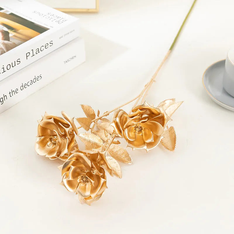 Gold plastic artificial flower arrangement featuring Persian eucalyptus and ginkgo leaves with single rose and peacock feathers
