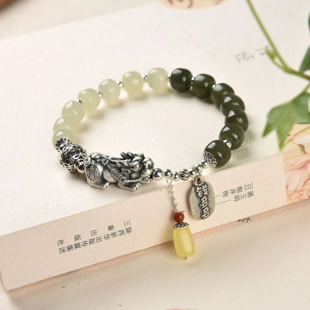 Close-up of a retro women's bracelet with a natural Hetian jade bead and a silver coin pendant on a wrist.