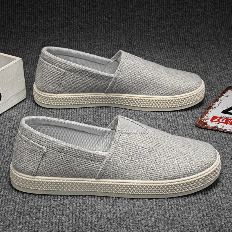 Men's beige linen canvas slip-on shoes with a round toe and shallow cut on a plain background.