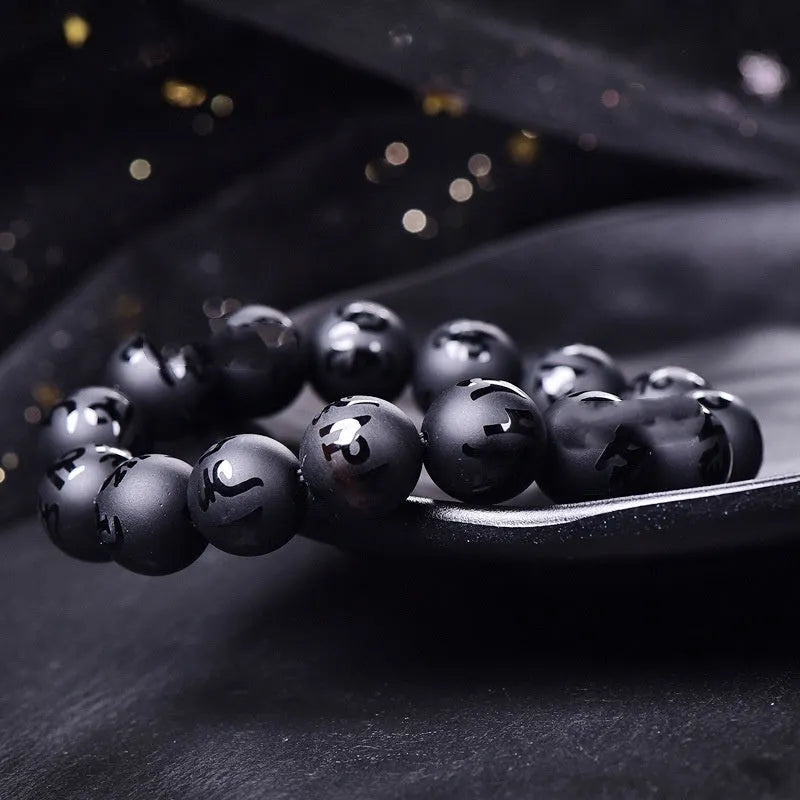 Natural frosted black agate Sanskrit mantra bracelet with Chinese style auspicious patterns on a wrist.