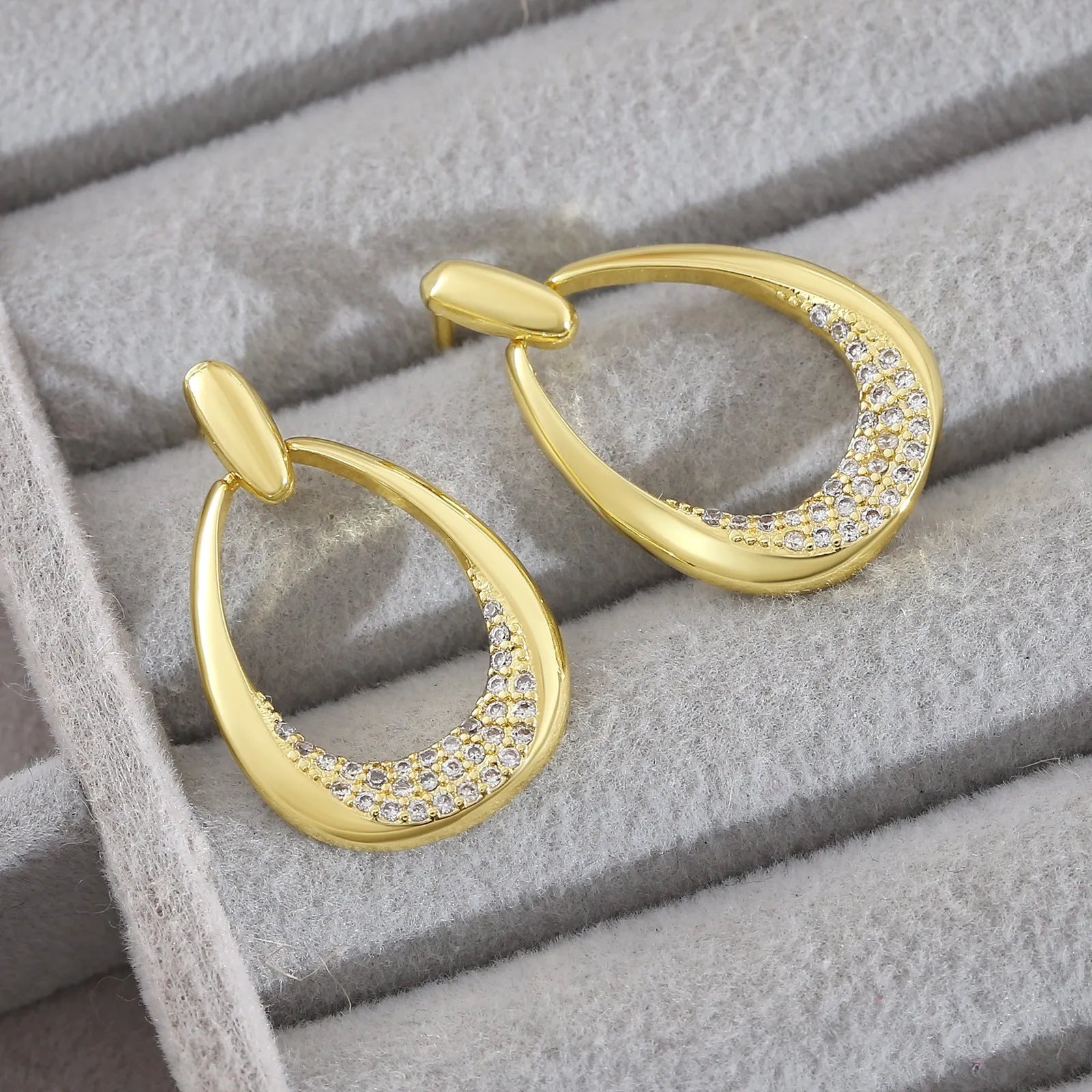 Yellow gold geometric drop-shaped women's earrings with round and oval ring elements on a simple background.