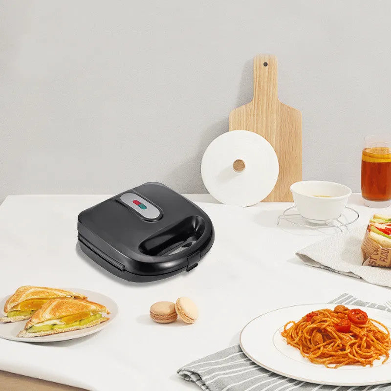 Black electric sandwich pan with double-sided heating and stainless steel lid on a kitchen counter.