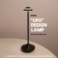 Metallic UFO-shaped rechargeable table lamp with touch controls in black finish on a wooden desk.