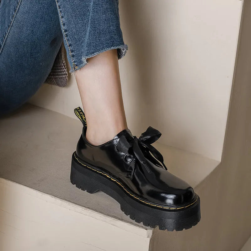 Black thick-soled women's leather shoes with cross-strap ribbons and lace-up closure on a white background.