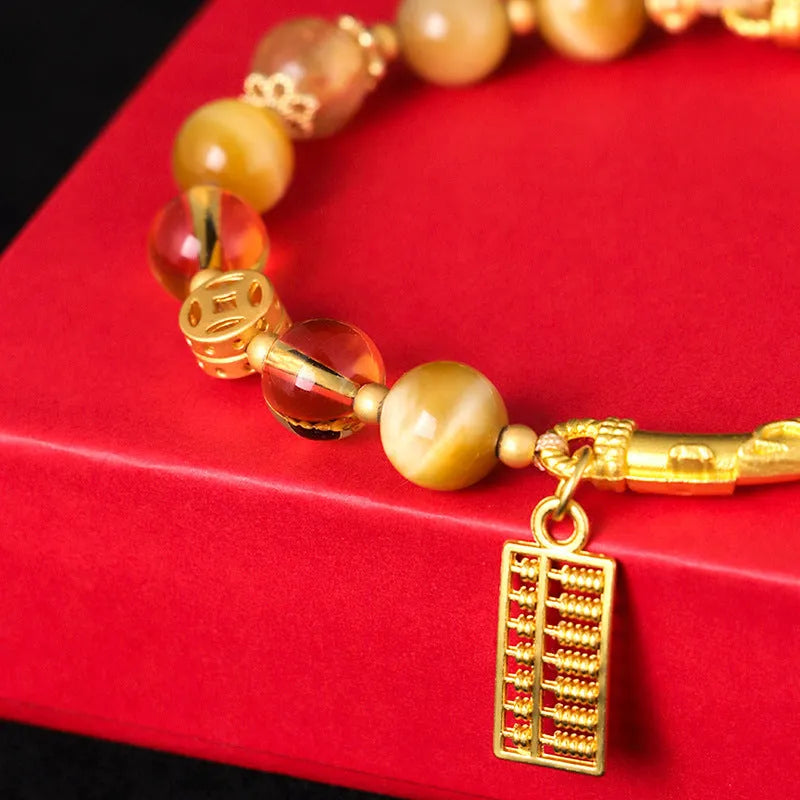 Close-up of a women's beaded bracelet with a diamond-shaped abacus tag bead, tigereye, citrine, and yellow tower crystal stones on copper.