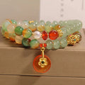 Gold-toned double ring chain bracelet with a peacock green agate safety buckle pendant and rhinestone details.