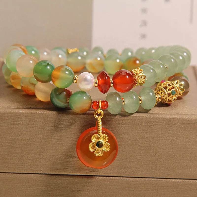 Gold-toned double ring chain bracelet with a peacock green agate safety buckle pendant and rhinestone details.