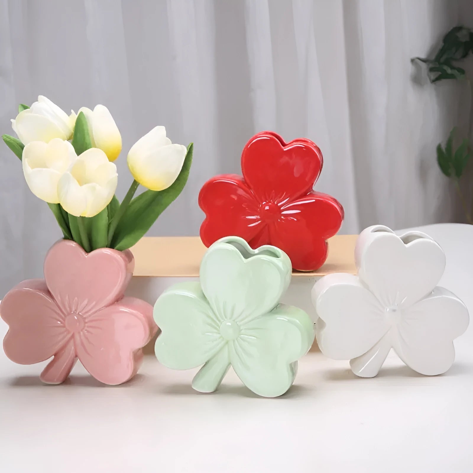 Small clover-design ceramic vase in pink, red, light green, or white on a desktop.