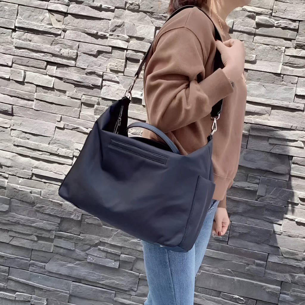 Black nylon waterproof shoulder bag with leather trim showing large main compartment