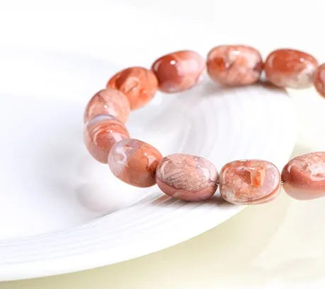 Natural cherry agate barrel bead bracelet with Ruyi charm on a white background.
