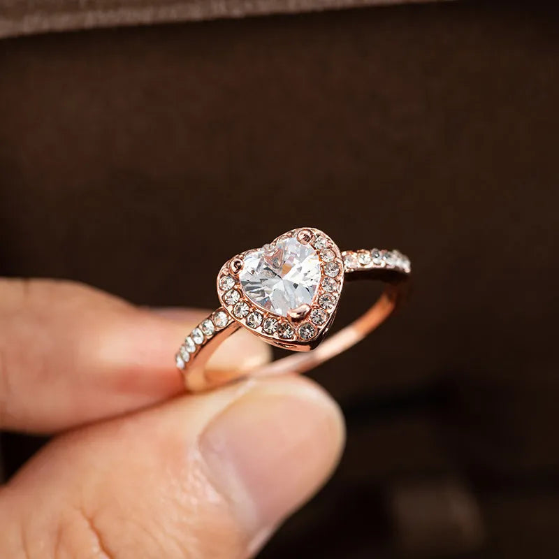 Women's heart-shaped wedding ring with central crystal on white copper band in rose gold finish.