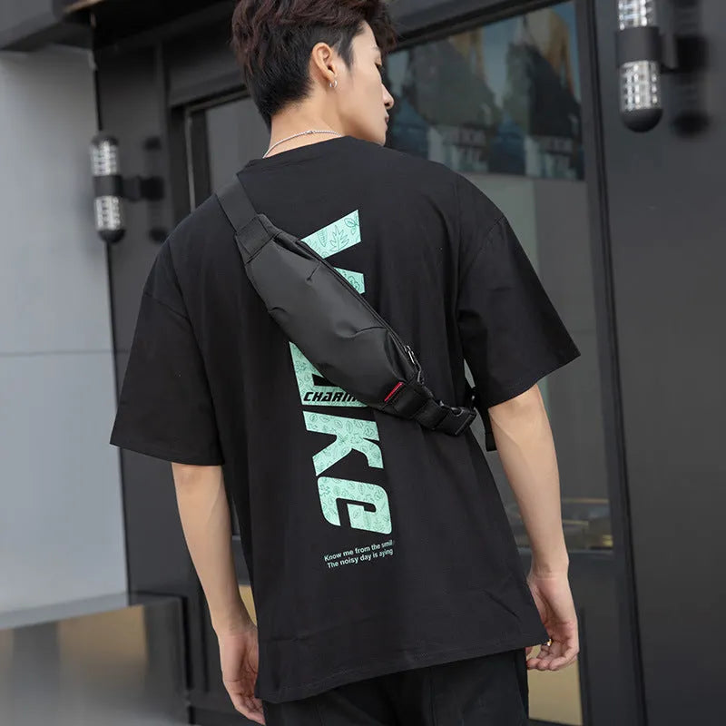 Black Oxford cloth waist pack for men worn crossbody, showing front zip and compact size.