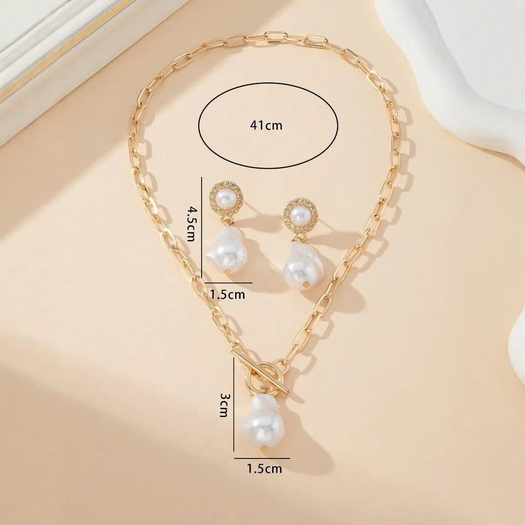 Gold tone retro style necklace and matching pearl ear studs set for women on a flat surface.