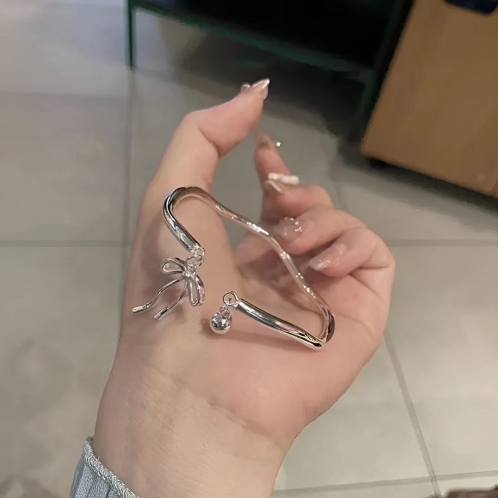 Silver adjustable bow bracelet with a bell opening clasp on a wrist.