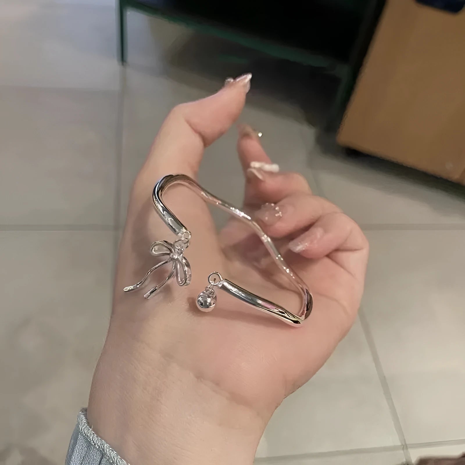 Silver adjustable bow bracelet with a bell opening clasp on a wrist.