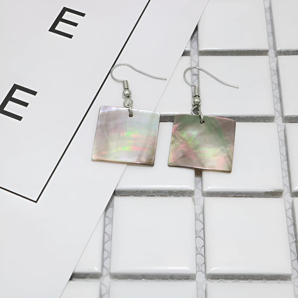 A pair of geometric shell earrings in a square panther design next to a rectangular shell design on a neutral background.