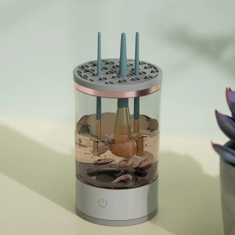 Grey and white electric makeup brush cleaner with USB charging cable on a wooden surface