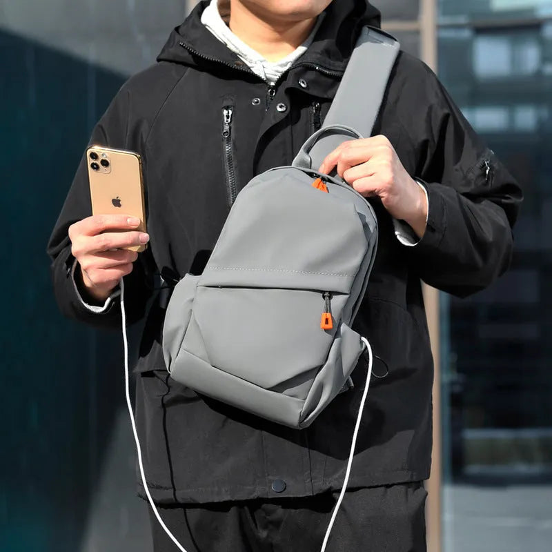 Men's black polyester crossbody bag with a single shoulder strap, shown in a casual setting.