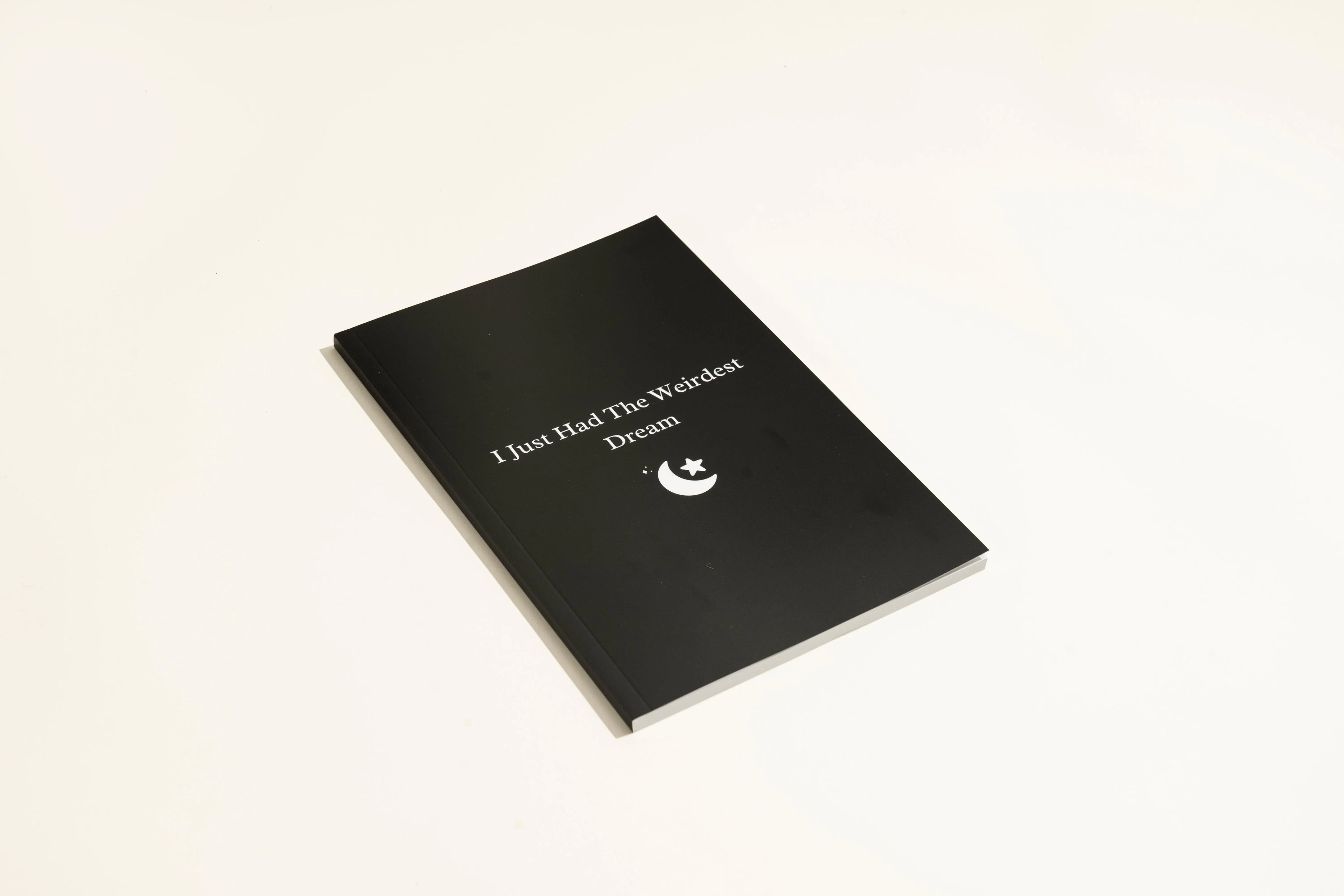 Black A5 hardcover dream journal with gold lettering, shown open on a lined page with a silk ribbon bookmark.
