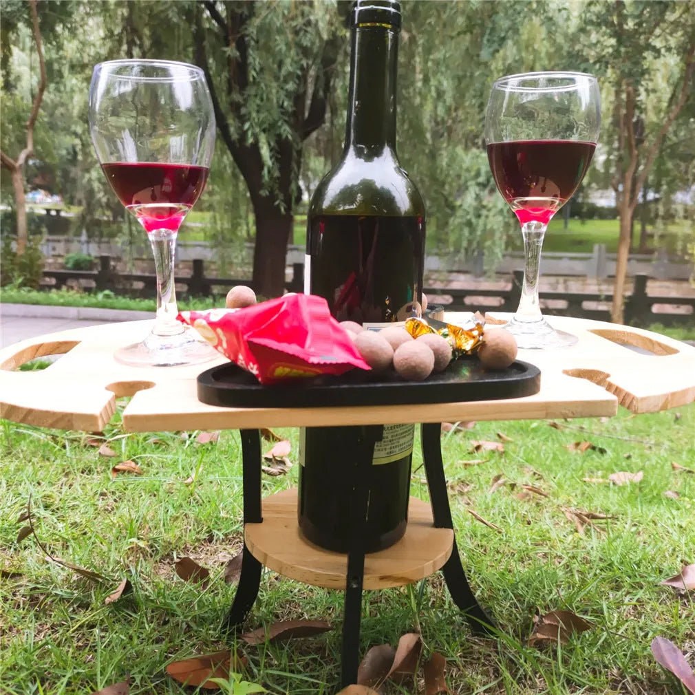Creative multifunctional white wood wine glass rack tray with bottle holder handle holding four wine glasses and a bottle on a picnic table