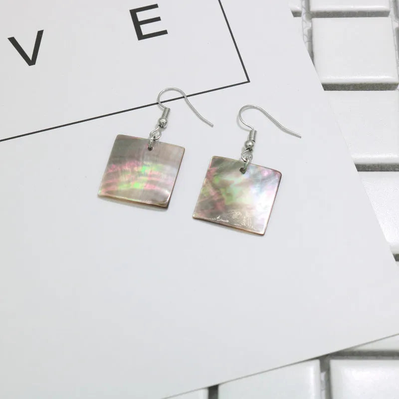 A pair of geometric shell earrings in a square panther design next to a rectangular shell design on a neutral background.