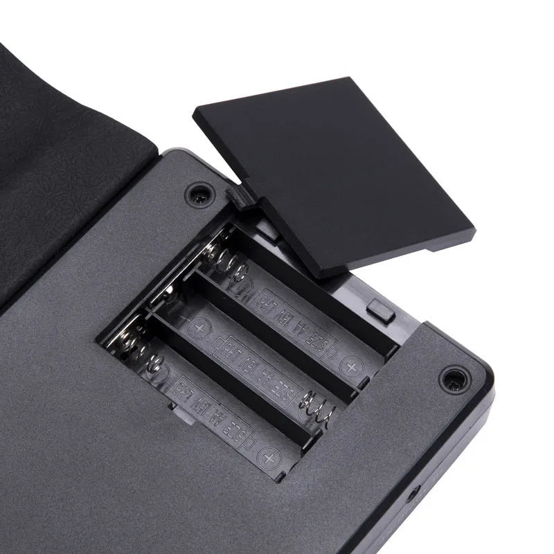 Compact folding electronic keyboard with 49 black silicone keys, shown in gloss black finish, rolled for storage next to its control panel.