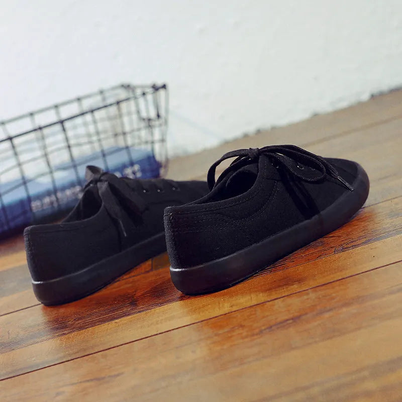 All-black low-top women's canvas shoes with flat rubber sole and lace-up front