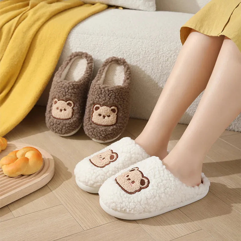 Pair of cute cartoon bear winter slippers with plush upper and non-slip TPR sole on a bedroom floor