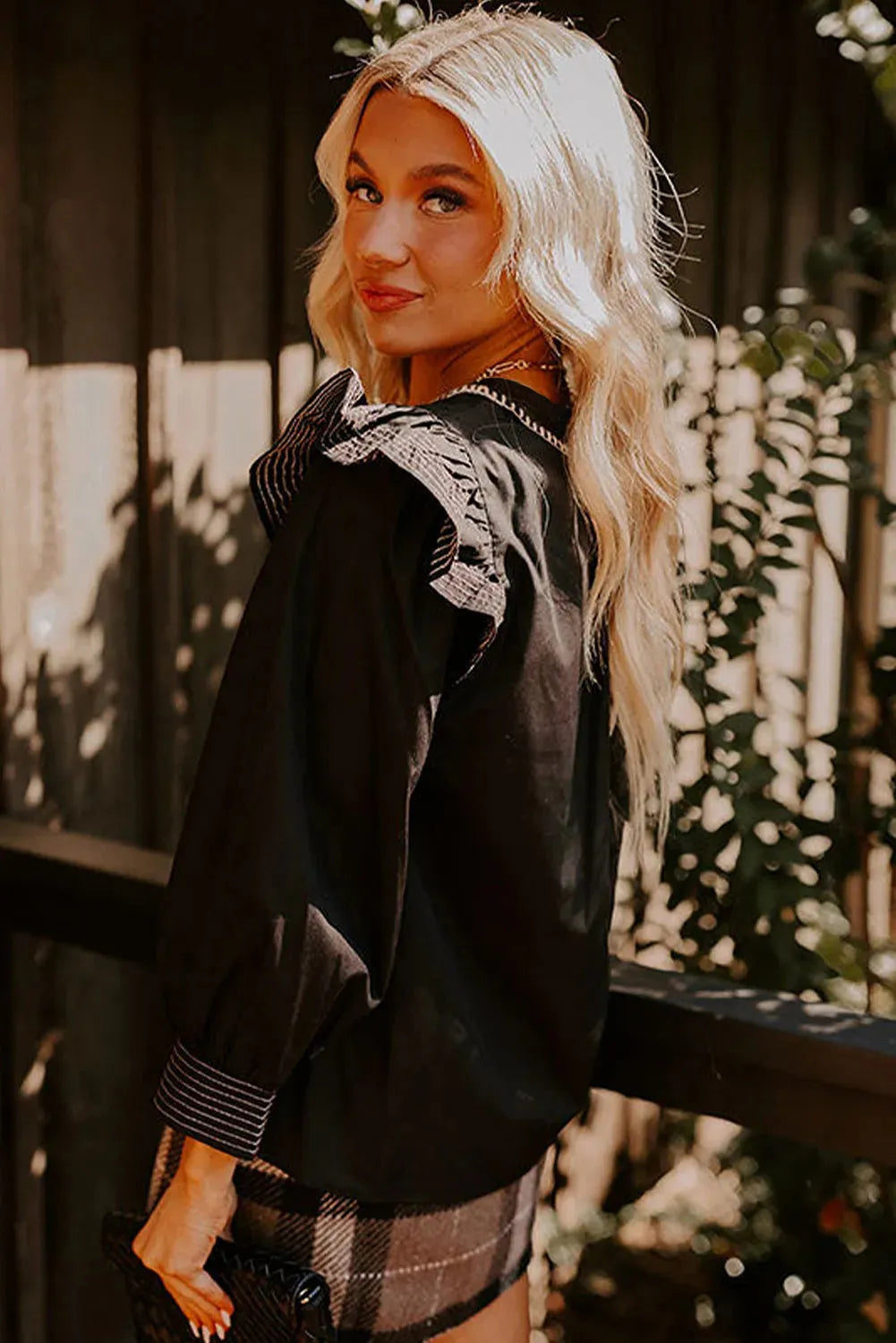 Black women's V-neck blouse with ruffled long sleeves and contrast stitching.