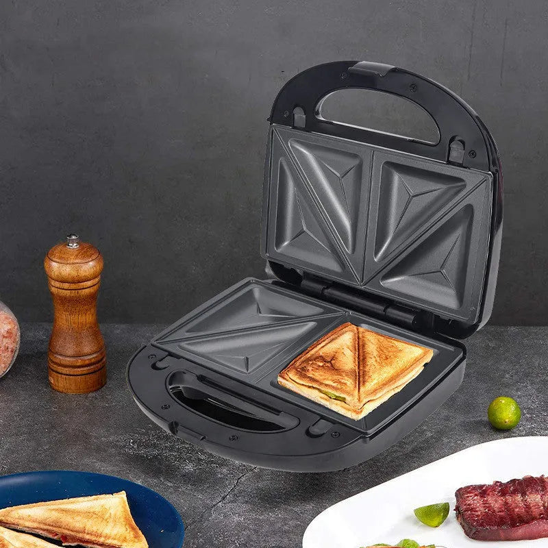 Black electric sandwich pan with double-sided heating and stainless steel lid on a kitchen counter.