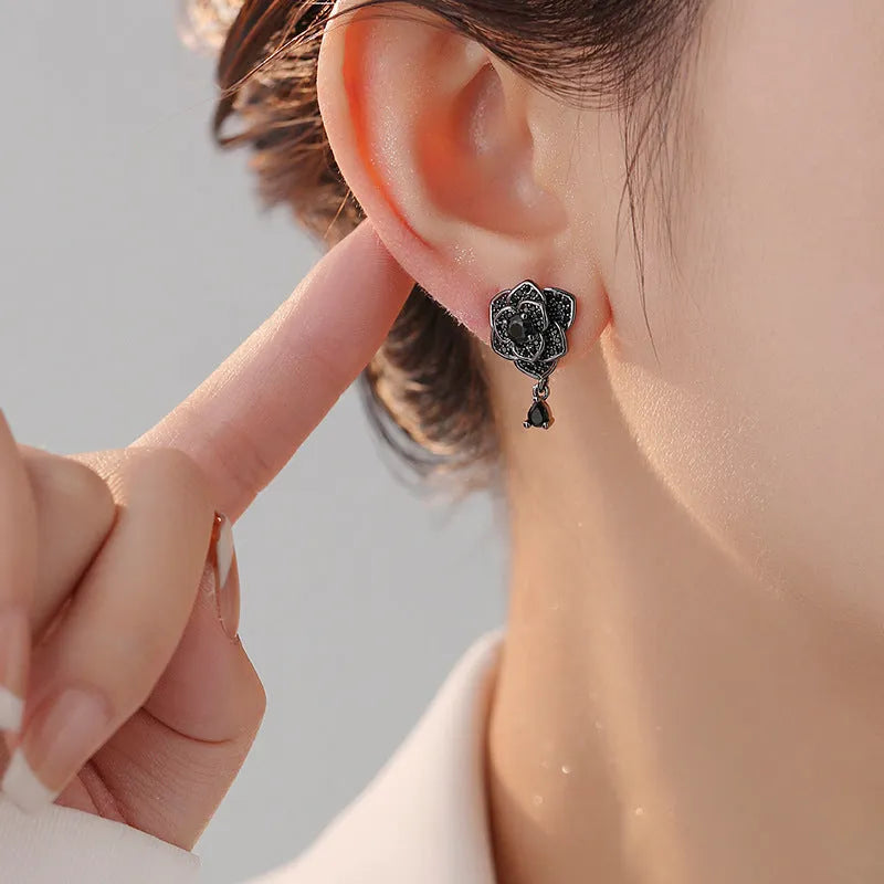 Close-up of women's black rose zircon flower stud earrings with 18K gold plating.