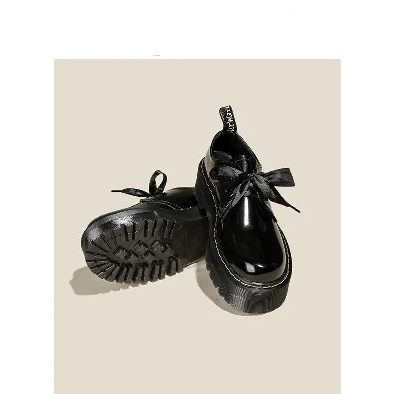 Black thick-soled women's leather shoes with cross-strap ribbons and lace-up closure on a white background.